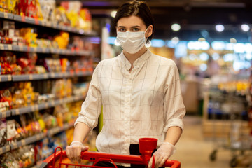 Young woman shopping in supermarket with shopping cart wearing medical face mask to protection the COVID-19 virus.