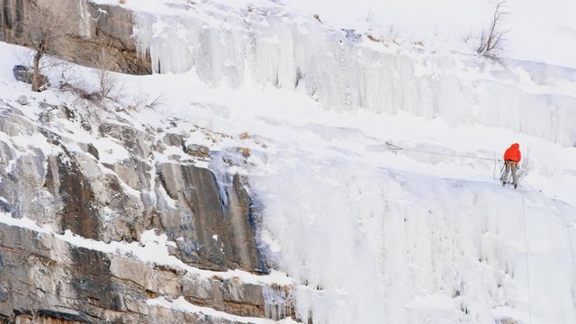 Pan across ice shelf on mountainside to reveal ice climber starting descent