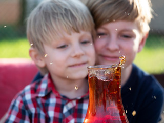 Two Caucasian boys watches a splash of tea in a cup from a falling piece of sugar