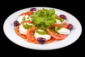 Tasty Caprese salad with peeled tomatoes, mozzarella, basil, and olives, on a plate, isolated on black background