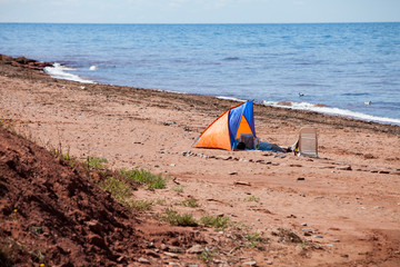 Man sleeping in and orange and blue tent on the red sand shores of Prince Edward Island in Canada.