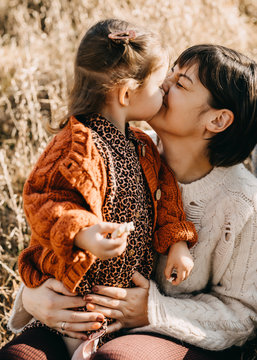 Mother and daughter playing outside on a sunny day. Mother kissing little girl.