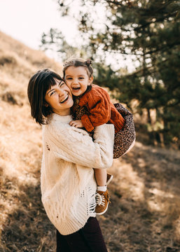 Mother and daughter playing outside on a sunny day. Mother hugging child, having fun together.