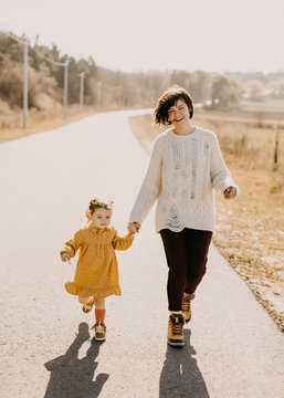Mother and child outdoors on a sunny day, walking or running together on an empty road.