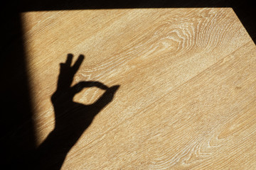 Shadow from a hand showing "ok" gesture on a wooden background. Okay, agree or perfect sign.