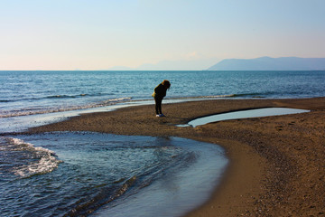 indistinct figure of lonely woman at the sea on the beach in winter at sunset