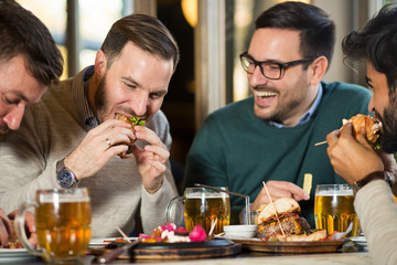Happy group of friends eating food and drinking beer at pub