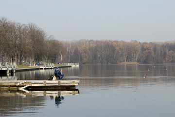 a man on the shore of a pier with a fishing rod catches fish on a city lake or river. City...