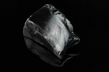 macro shot of an obsidian stone mineral specimen in it's raw form on a reflective black background