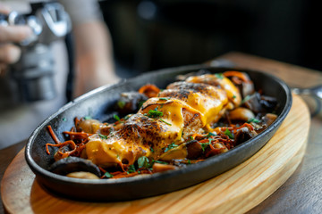 Chicken with grilled cheese on top, over a metal pan and wooden cutting board