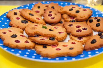 Homemade cookies decorated with berries, raisins and colored candied fruits on a blue plate at yellow background