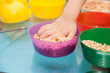 Hand of a small child playing with dry peas and semolina in multi-colored bowls