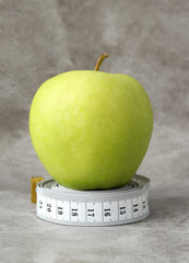 A green delicious Apple stands on a white measuring tape, rolled into a ball. Selective focus. Weight and nutrition control.