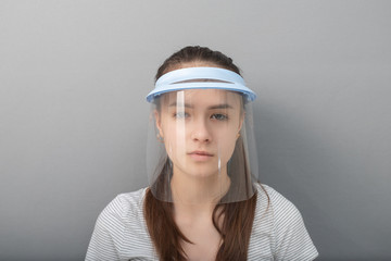 Young woman in a protective mask screen with a visor on a gray background