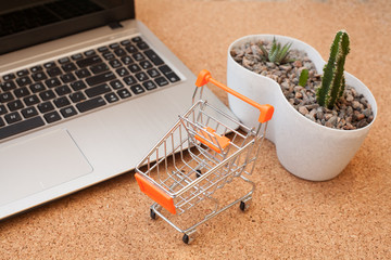 A small orange cart stands next to a laptop this image implies online shopping, that the customer order things from retail sites over the Internet.
