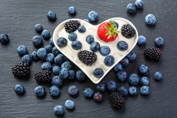 Blackberries, strawberries and blueberries with cream in a white plate in the shape of a heart