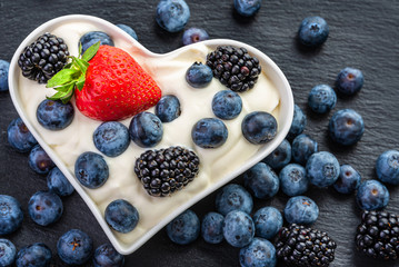 Blackberries, strawberries and blueberries with cream in a white plate in the shape of a heart