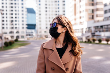 Beautiful woman wearing protective medical mask walking on the city street during the epidemic