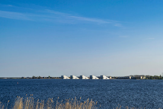 Blue seascape with bright blue water of lake Gooimeer and white modern nautical-style houses on the horizon. Interesting attractions for domestic vacation tourism in Netherlands, Dutch town Huizen. 