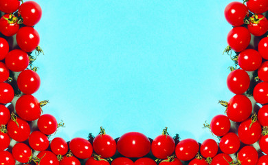Red cherry tomatoes over blue background, horizontal image. Colorful food background. Advertising, menu, food ingredients concept. Frame of red cherry tomatoes on a blue background.
