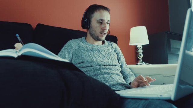 Hermoso joven trabajando con una computadora port&aacute;til mientras est&aacute; sentado en la sala de estar tomando caf&eacute; durante la cuarentena debido al virus covid-19