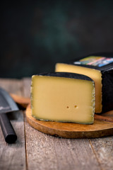 Medium hard cheese head gouda edam on wooden board with knife wooden texture daylight