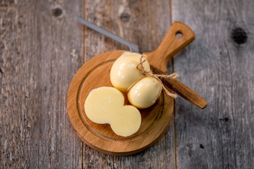 Medium hard cheese head scamorza on wooden board with knife wooden texture daylight