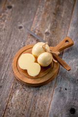Medium hard cheese head scamorza on wooden board with knife wooden texture daylight