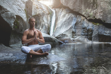 young athletic boy doing iodine and meditation in a waterfall