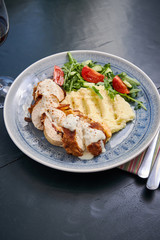Chicken breast stuffed with cheese and mashed potatoes on the side with some red wine on a table