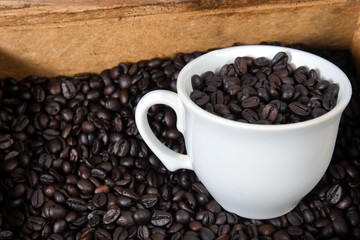 cup with roasted coffee beans inside, on the table with roasted beans