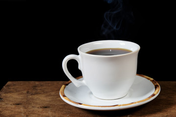 cup of hot coffee with smoke. over wooden table on black background.