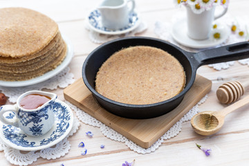 Home made raw vegan pancakes on a white table with honey and hazelnut. Healthy morning meal in a black a frying pan.