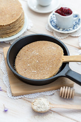 Home made raw vegan pancakes on a white table with honey and hazelnut. Healthy morning meal in a black a frying pan.