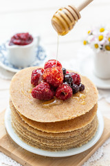 Honey dripping form a wooden honey spoon on to raw vegan pancakes with raspberries on a white table.