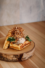 Presentable plating of Belgian waffle topped with thin sliced onion crisp and white sauce on a wooden chopping board. Food photography concept for magazine or online delivery menu.
