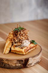 Presentable plating of Belgian waffle topped with thin sliced onion crisp and white sauce on a wooden chopping board. Food photography concept for magazine or online delivery menu.