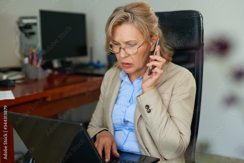 Wall mural portrait of mature female boss talking on phone in office.