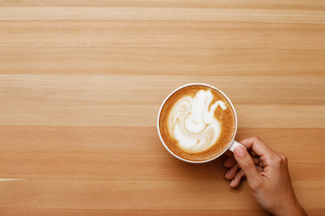 Coffee latte with in hand nice and presentable plating in a white mug top view in wooden table background. Hot beverage photography with space available for text.