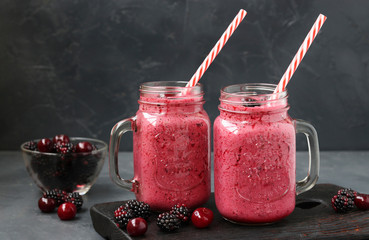 Two servings of homemade smoothies with natural yogurt, blackberries and cherries in glasses on dark background, Diet and weight loss control concept, Closeup