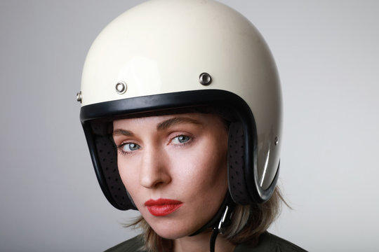 Portrait of biker young woman, wearing white helmet, looking straight at the camera with red lips. Studio background.