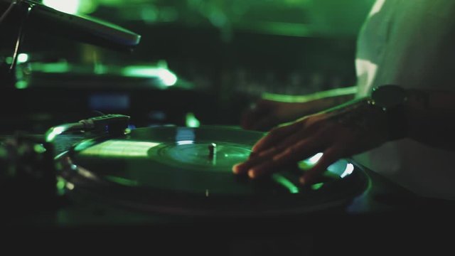 Modern style of music, front view of man with tattoo on the hand plays on the electronic musical device for djs with colorful illumination