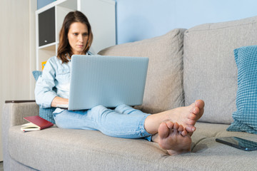 Casual beautiful woman working on a laptop lying on the bed in the sofa. Working from home. Stay at home concept. Focus on foot