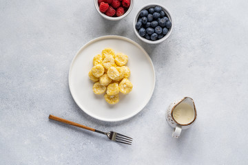 Delicious lazy dumplings served with fresh berries on a white plate, placed against a neutral gray...