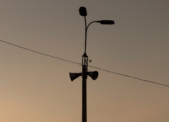 Outline of a pillar with wires, tape recorders, lamps against the sky