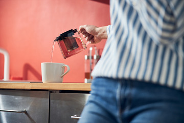 Fototapeta na wymiar Caucasian lady pouring tea in kitchen at home