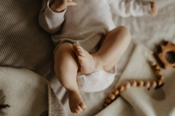 legs of a baby lying on a beige plaid and wooden toys on the background