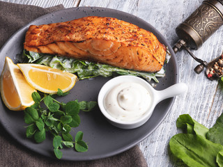 roasted baked salmon fillet with lemon, white sauce and spinach close up
