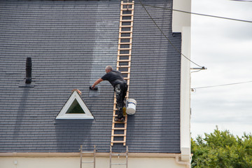 Worker spreading a product on a roof with a roller