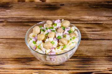 Salad with marinated mushrooms, sausage, onion, boiled potato and mayonnaise on a wooden table